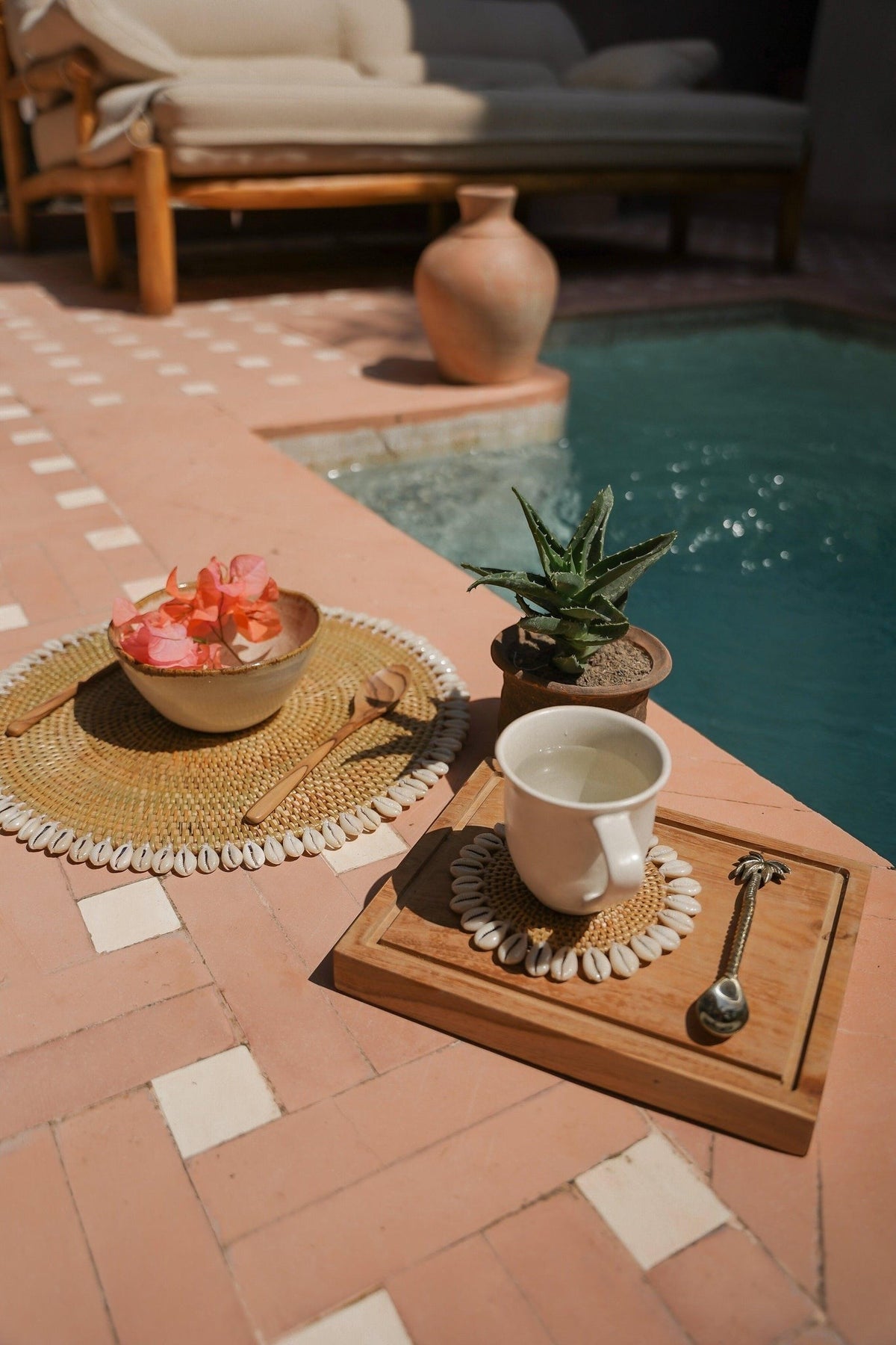 Kayu Living gold brass spoon with palm tree design on a wooden board next to a cup by a pool