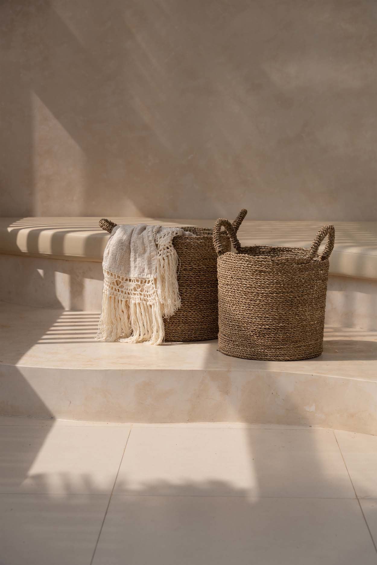 Kayu Living Gypsy Bed Throw in natural cotton with fringe detail draped over a woven seagrass basket