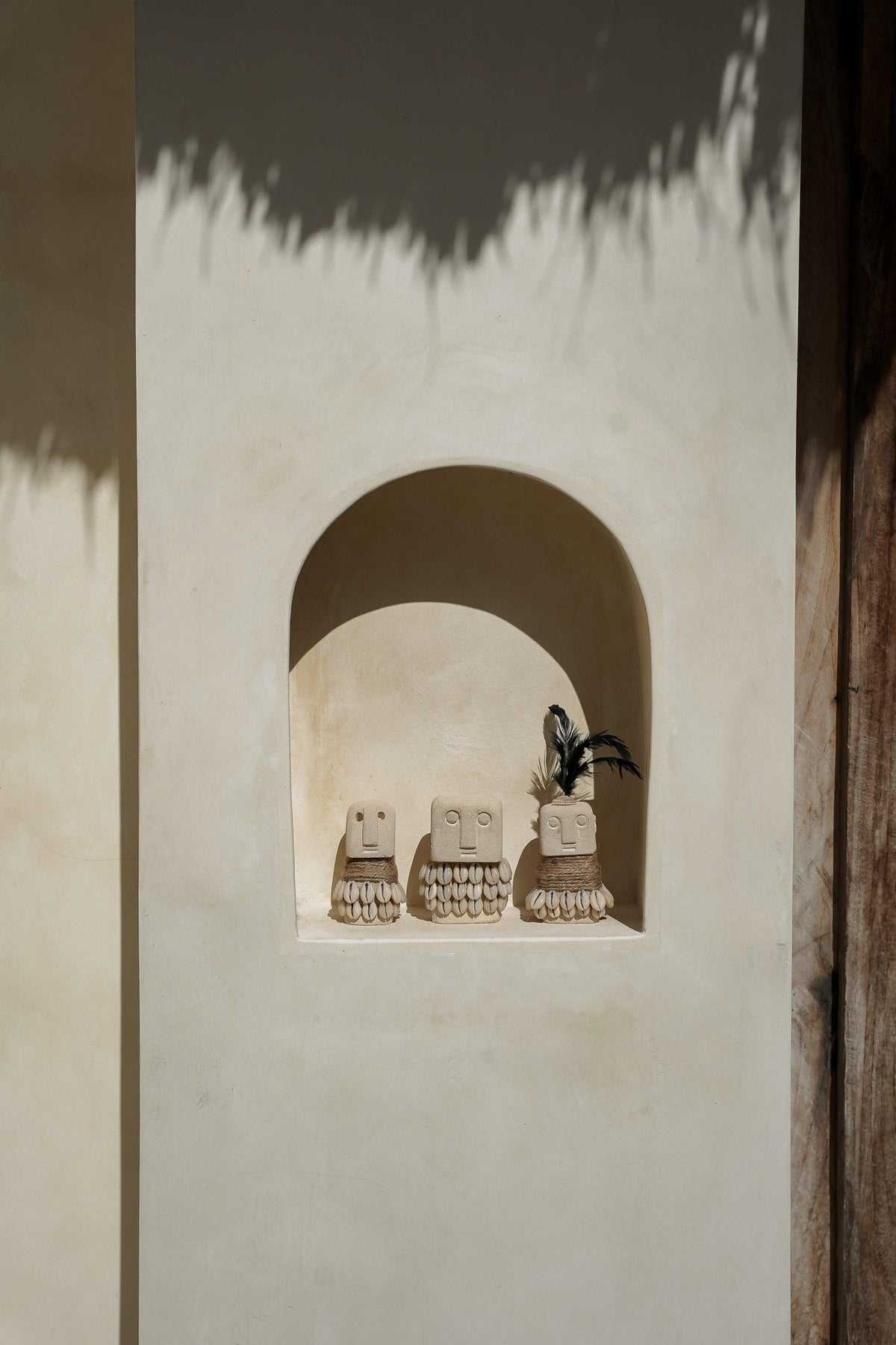 Three Kayu Living handmade stone figurines with carved faces and rope details displayed in a wall niche.