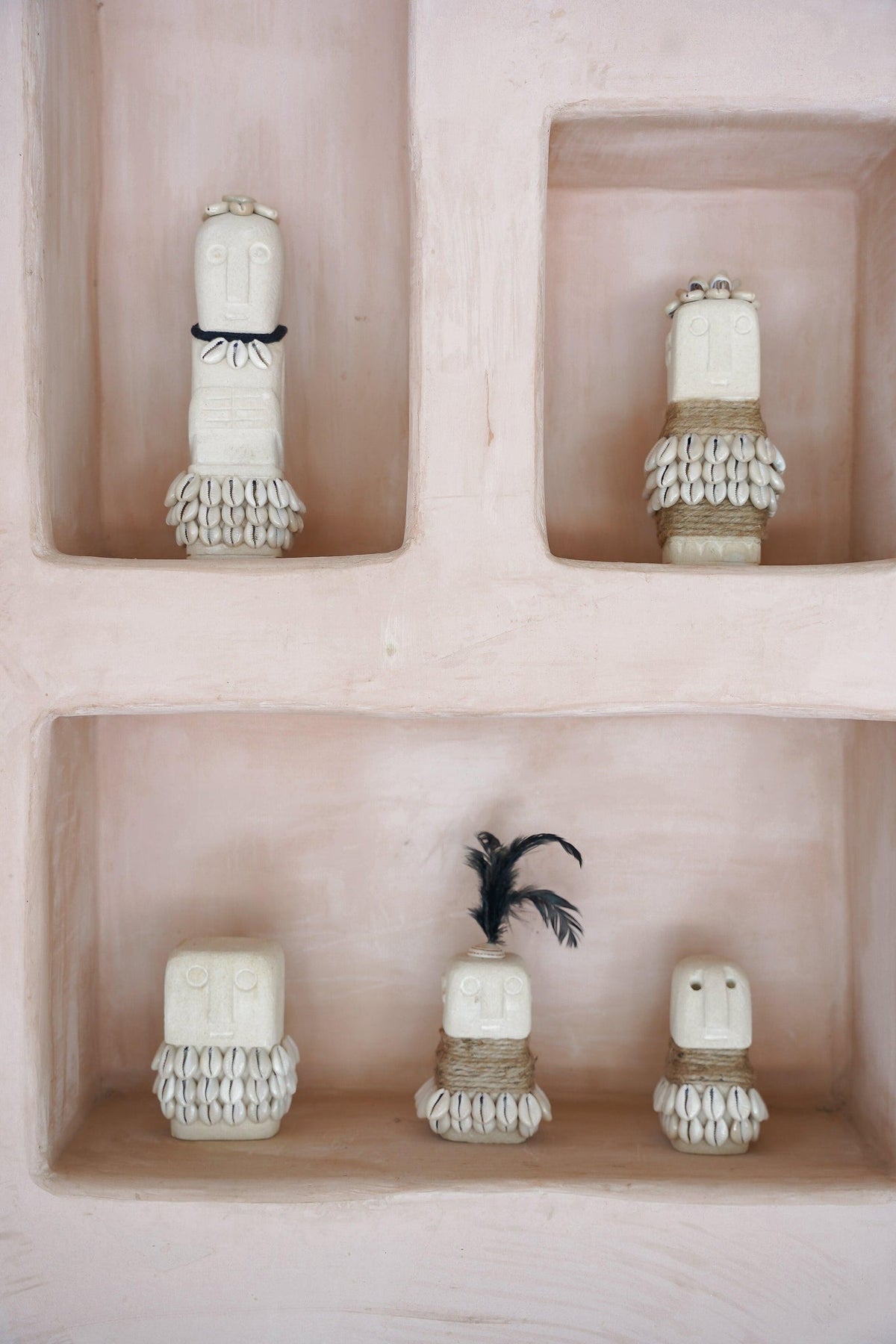 Kayu Living handmade stone figurines decorated with shells and feathers displayed in a pink wall niche.
