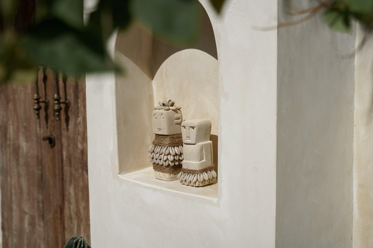 Kayu Living handmade stone figurines with shell and rope accents displayed in a white arched wall niche.