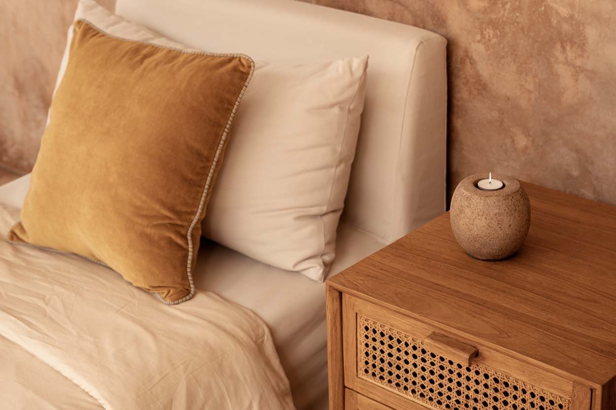 Kayu Living Harmony nightstand in solid teak with handwoven rattan drawer fronts beside a cozy neutral bed.