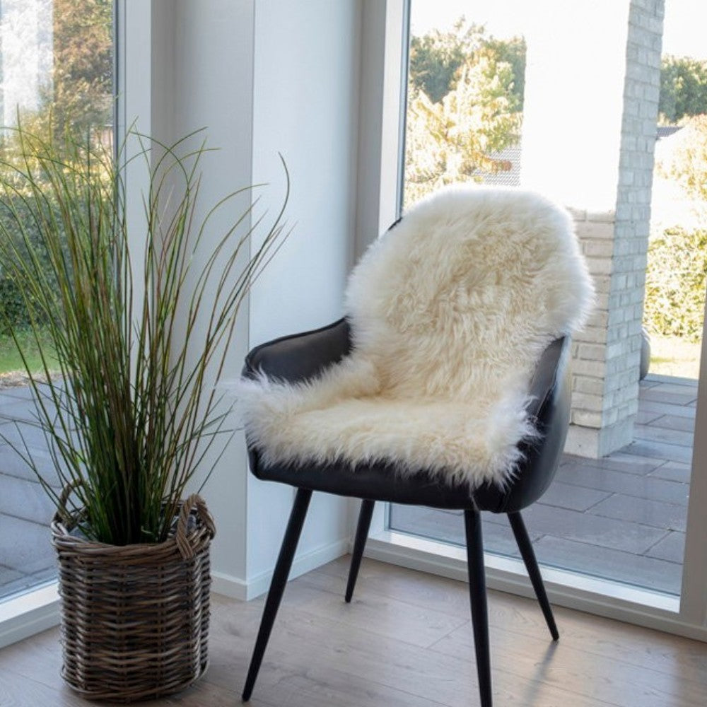 Kayu Living ivory lambskin throw draped over a modern black chair in a bright, sunlit room.