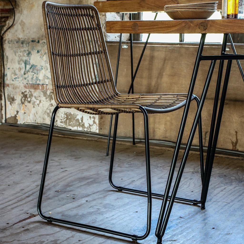 Kayu Living Jane natural synthetic rattan garden chair with a black metal frame in a rustic indoor dining setting.