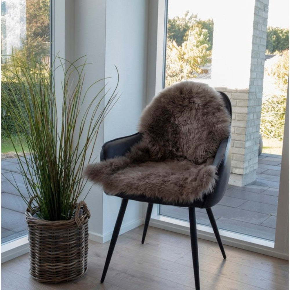 Kayu Living mushroom coloured genuine lambskin rug draped over a modern black dining chair in a bright room.