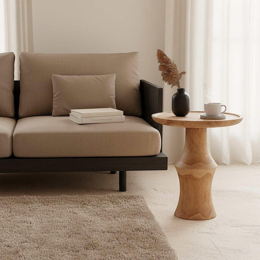 Kayu Living Nero Dawn side table in natural teak wood with a sculptural pedestal base next to a modern sofa