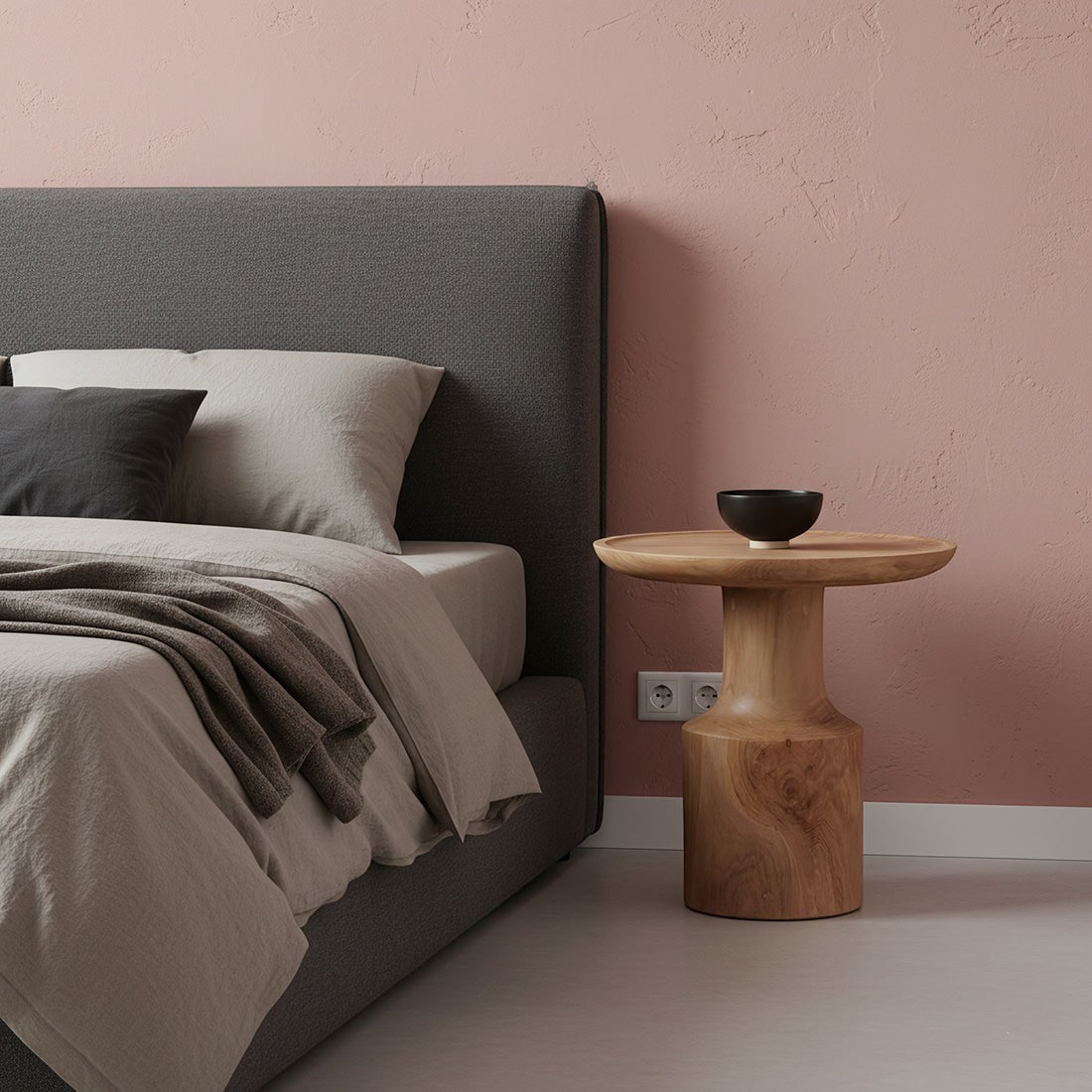 Kayu Living Nero Day teak side table with a natural wood finish beside a grey upholstered bed in a pink bedroom.