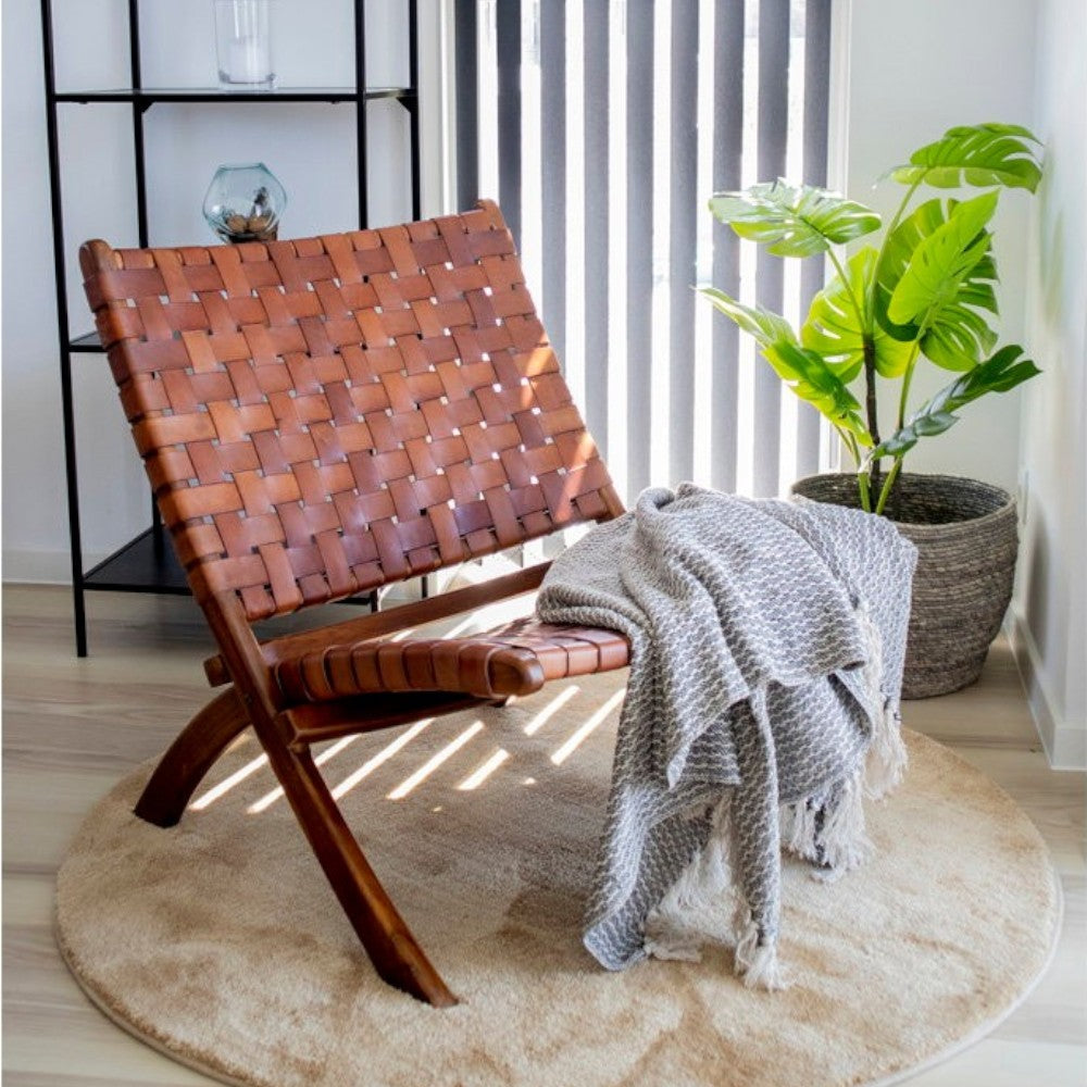 Kayu Living Perugia folding chair with brown woven leather seat and teak wood frame in a modern living room setting.
