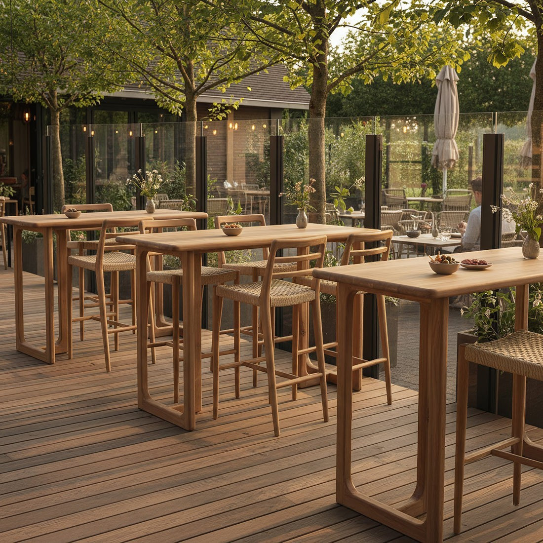 Kayu Living Primavera teak bar tables with rounded tops and U-shaped legs on an outdoor wooden terrace.