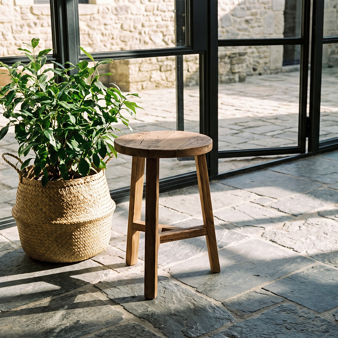 Kayu Living brown reclaimed wood stool with unique grain patterns, used as a rustic side table on a stone patio.