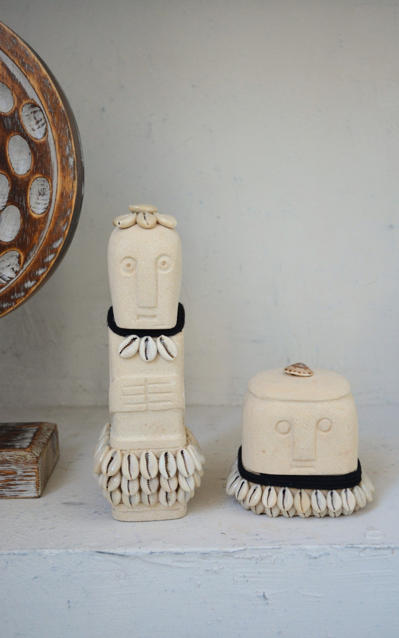 Kayu Living handmade stone figurines decorated with cowrie shells and black fabric accents on a white shelf