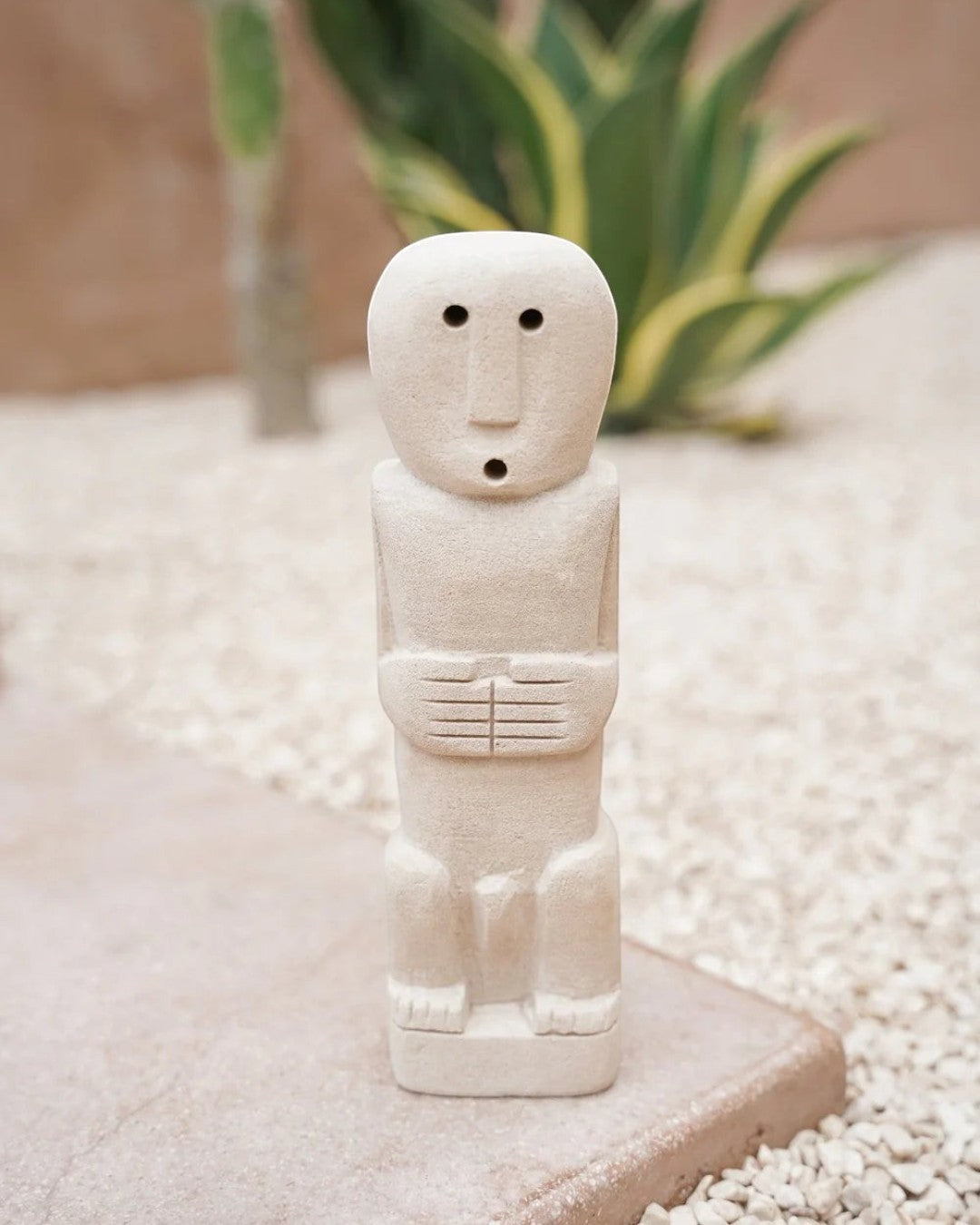 Kayu Living handmade natural stone gatekeeper figurine with minimalist carved features on a gravel surface.