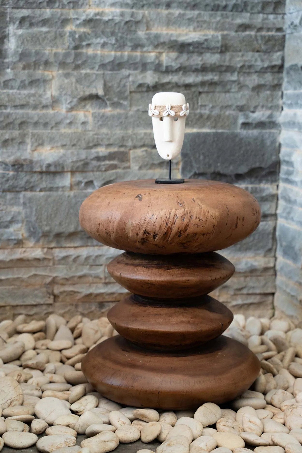 Kayu Living hand-carved sandstone Sumba figure with shell detail on a wooden stand against a stone wall background