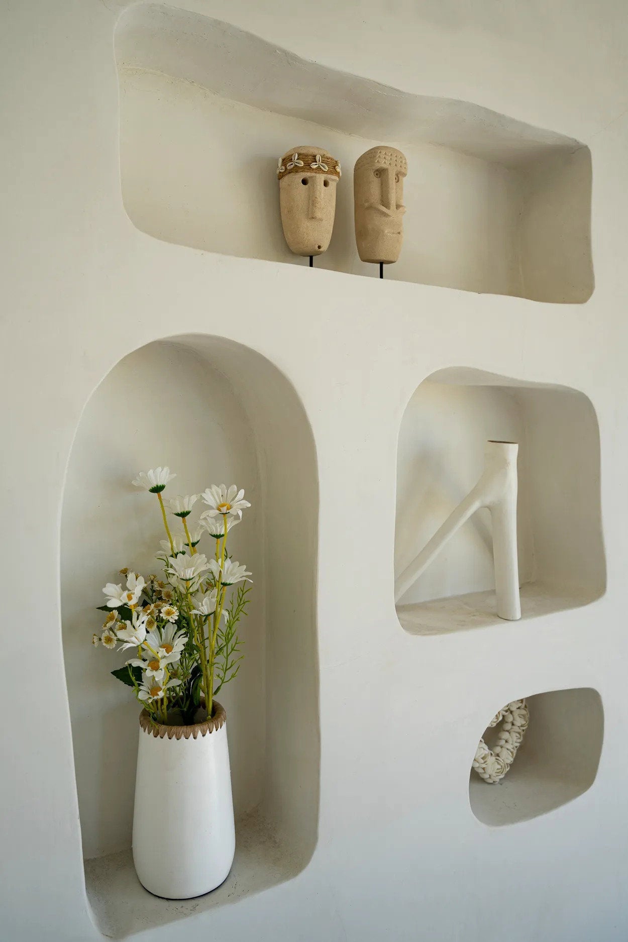 Kayu Living hand-carved sandstone Sumba stone figures with shell detail displayed in a white arched wall niche