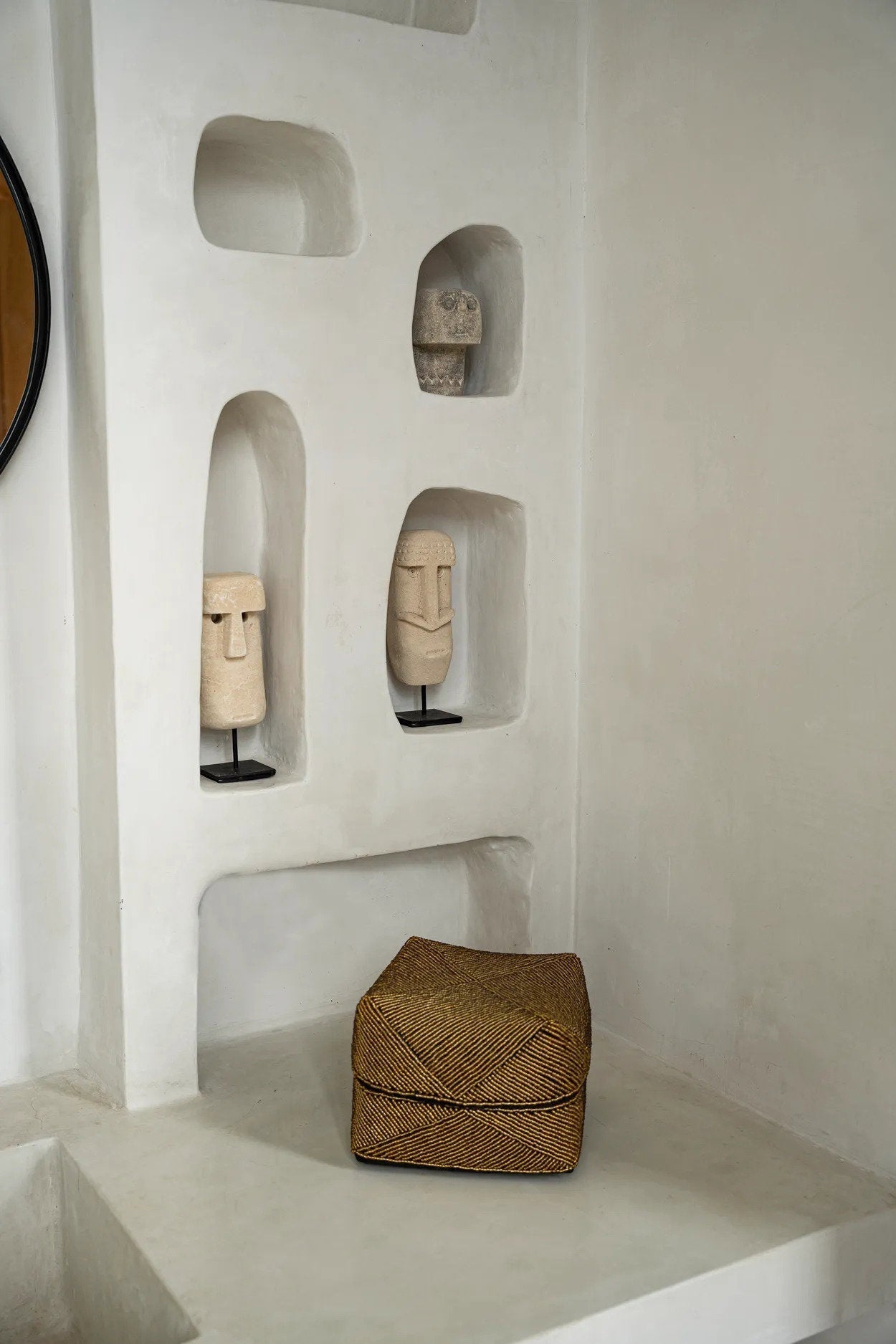 Kayu Living hand-carved sandstone Sumba statue on a black metal stand displayed in a white arched wall niche.