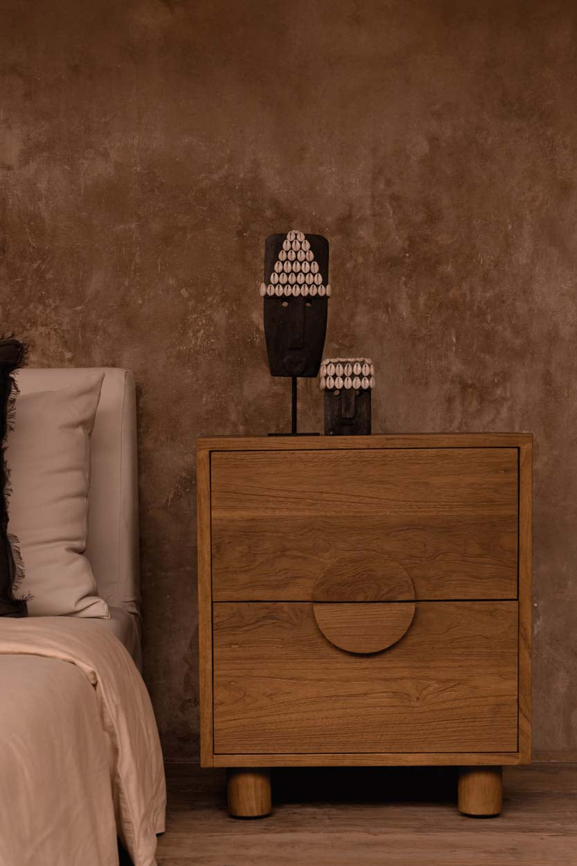 Kayu Living hand-carved grey sandstone Sumba stone statue on a metal stand displayed on a wooden bedside table.