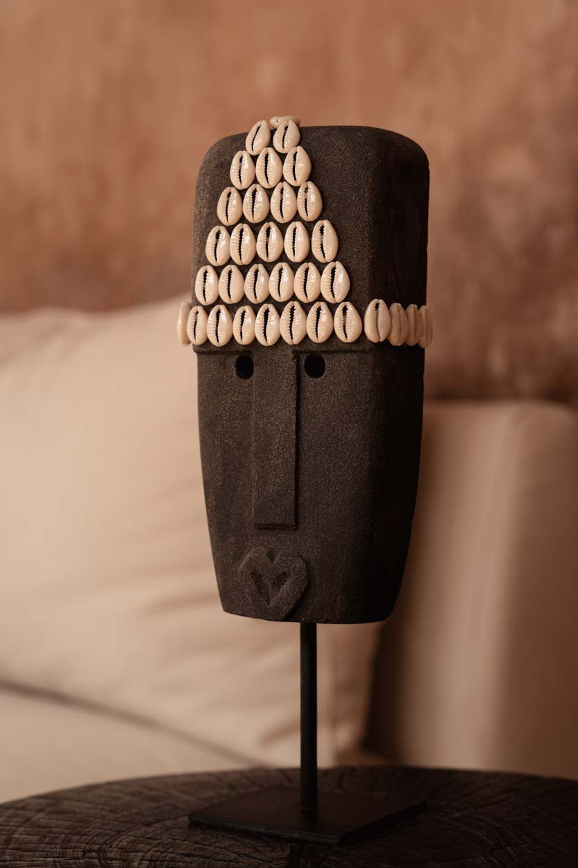 Kayu Living hand-carved grey sandstone Sumba statue on a metal stand, decorated with traditional cowrie shells.