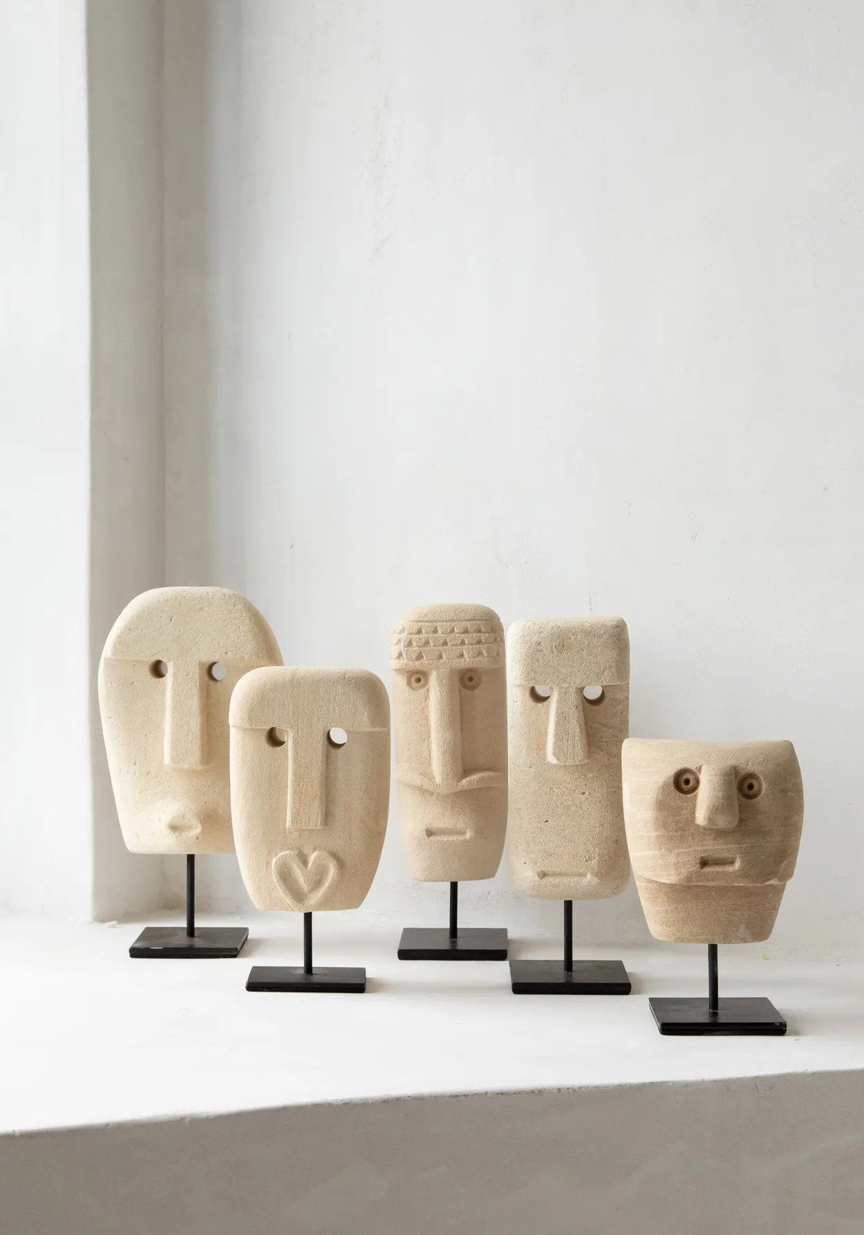 Kayu Living hand-carved sandstone Sumba stone statues on black metal stands, featuring unique tribal face designs.