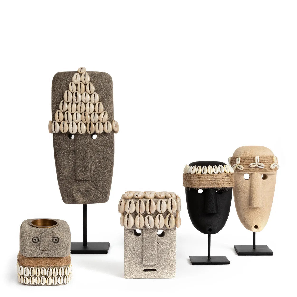 Kayu Living collection of hand-carved Indonesian sandstone statues with cowrie shell accents on black metal stands.