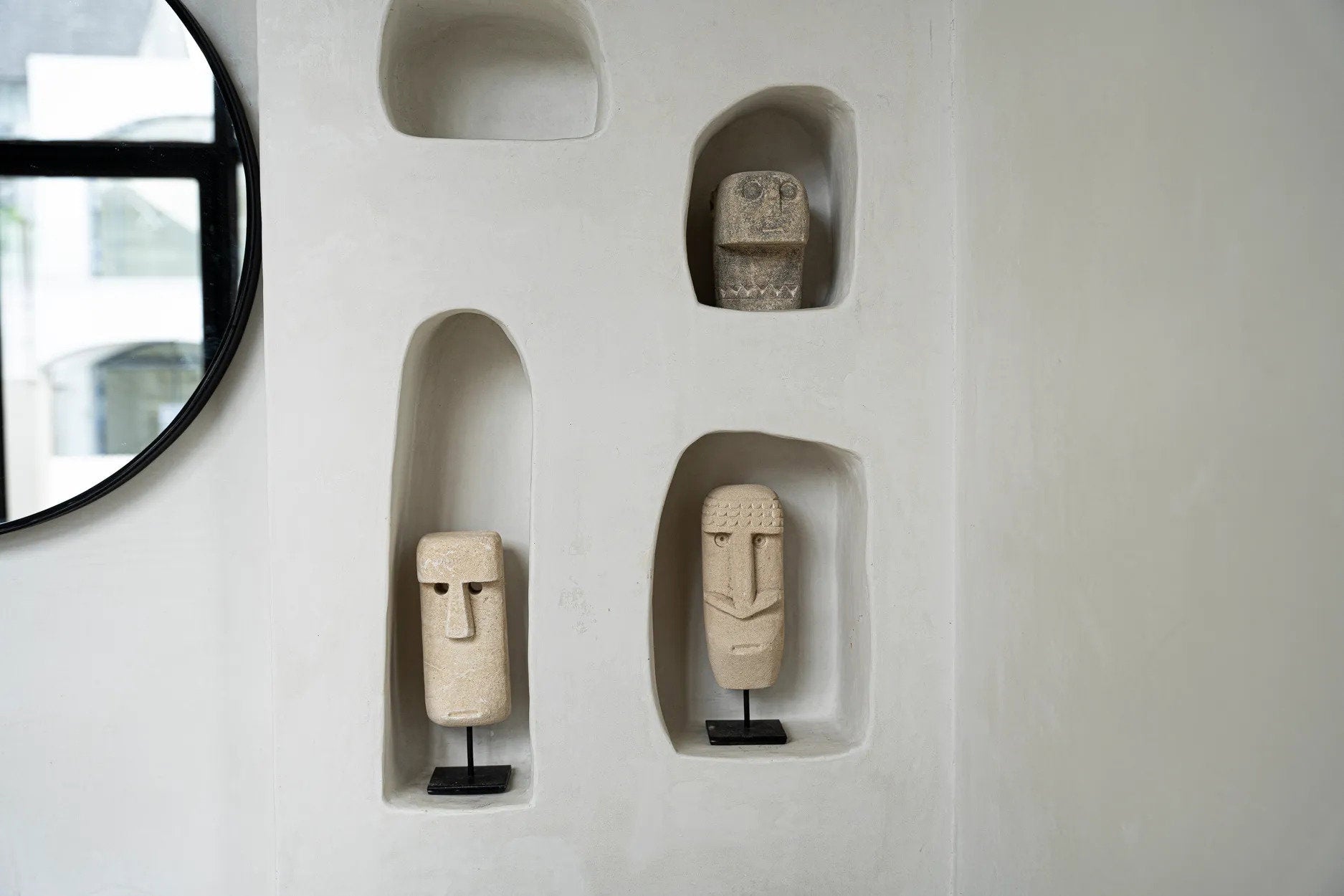 Kayu Living hand-carved Sumba sandstone statues on black stands displayed in white wall niches for rustic decor