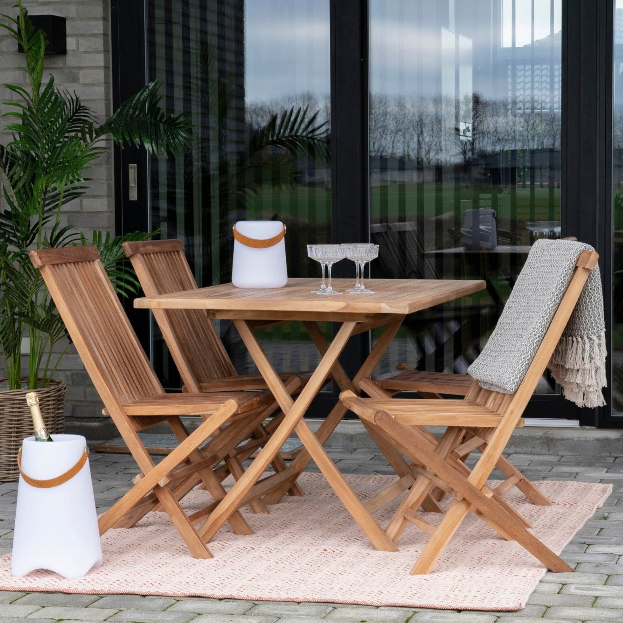 Kayu Living Toledo natural teak wood folding dining chairs set on a patio with a matching square table
