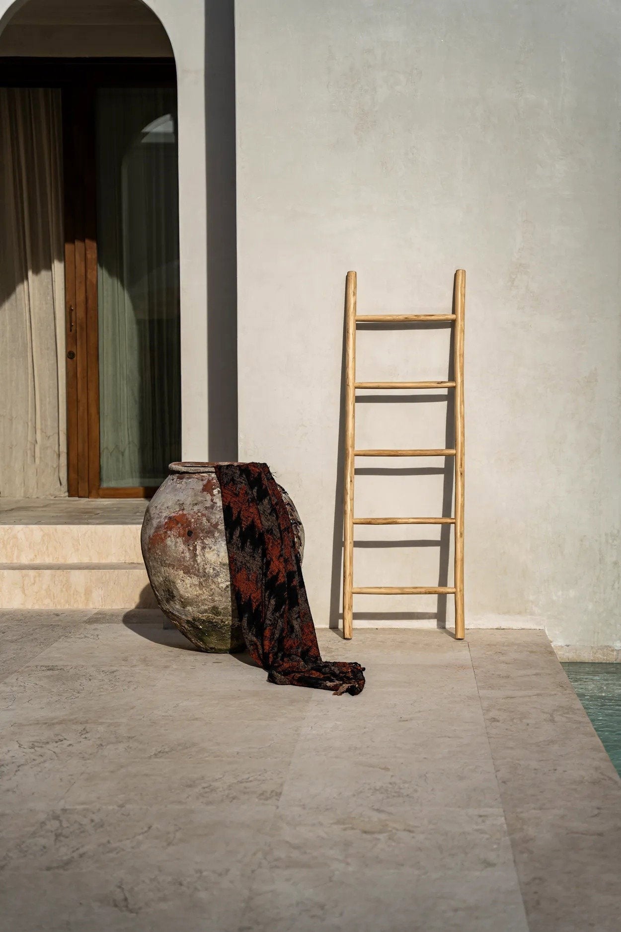 Kayu Living Tulum teak wood decorative ladder leaning against a neutral wall next to a large rustic clay pot