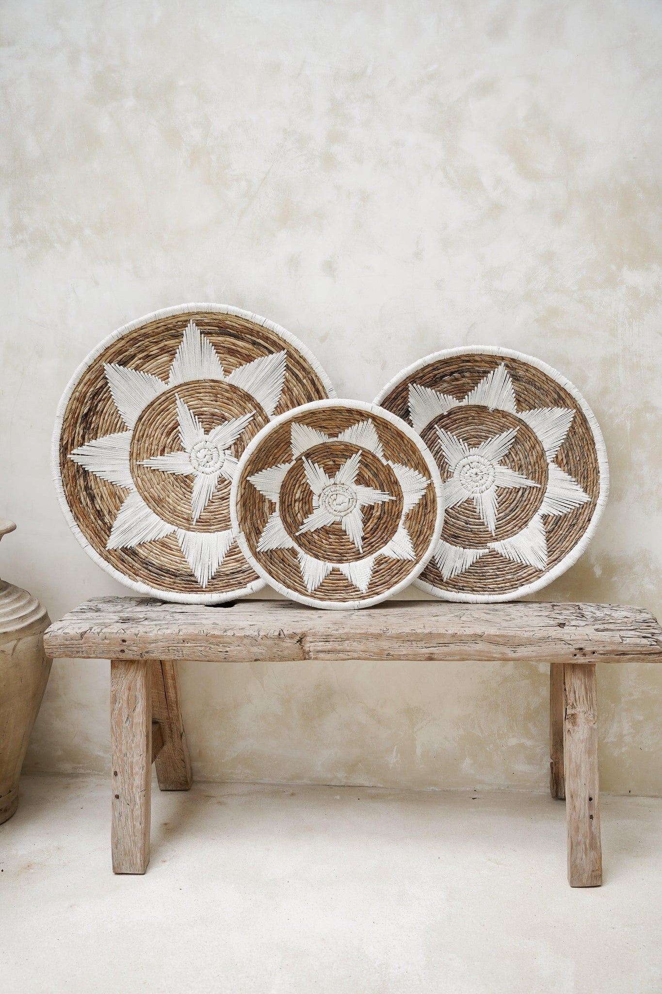 Kayu Living Uluwatu handmade banana-leaf and cotton wall baskets in brown and white with star patterns on a wooden bench