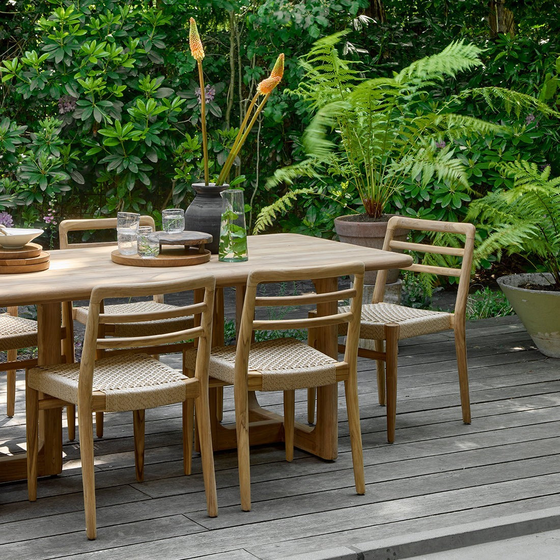 Kayu Living Verano teak dining chairs with woven rope seats arranged around a wooden table on a garden deck.