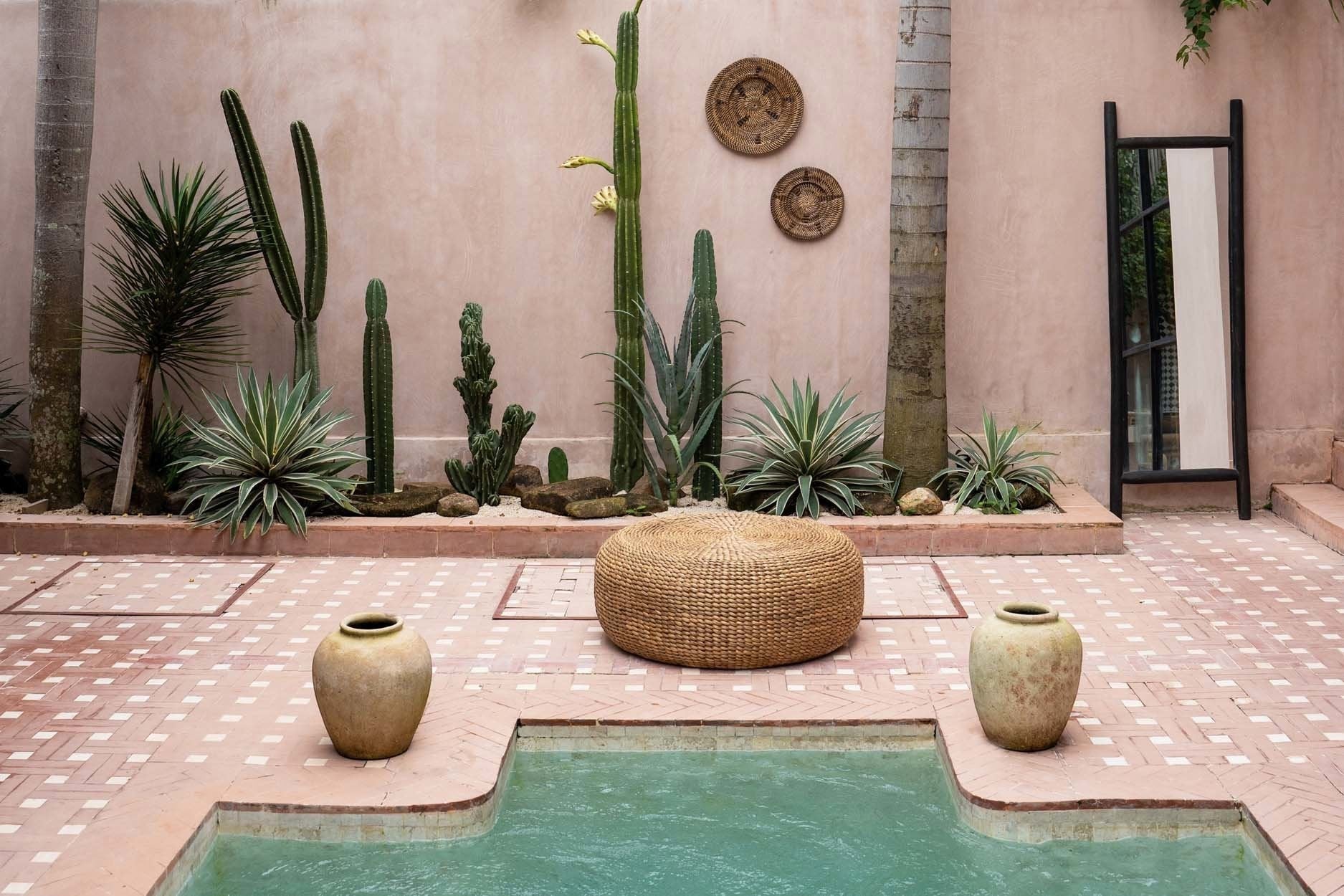 Kayu Living natural water hyacinth pouf in a desert-inspired outdoor courtyard with cacti and a small pool.